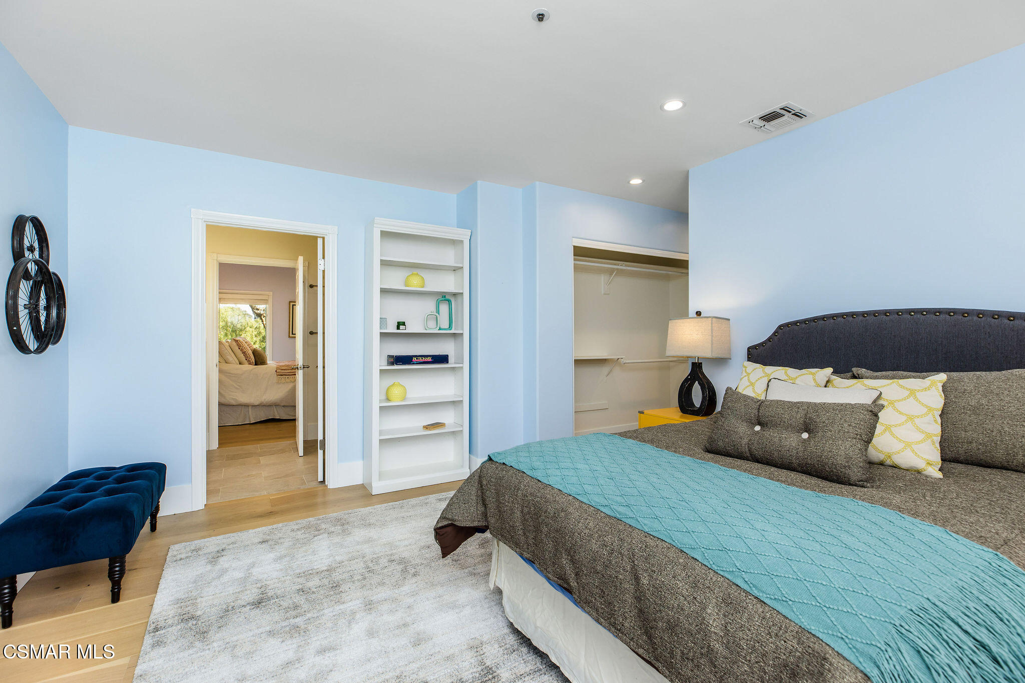Bedroom with a gray upholstered bed, turquoise coverlet, built-in shelves, and an open closet.