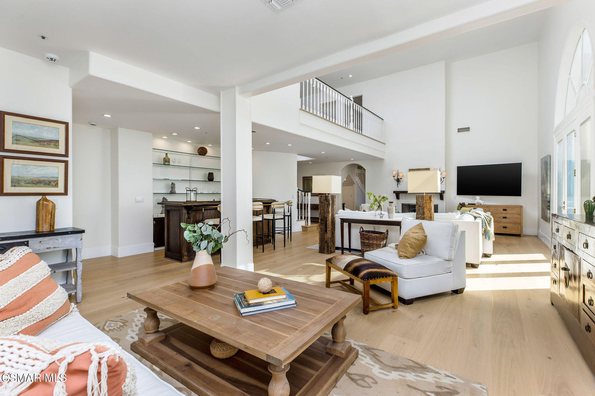Double-height living room with white sofas, a wood coffee table, and an upstairs balcony.
