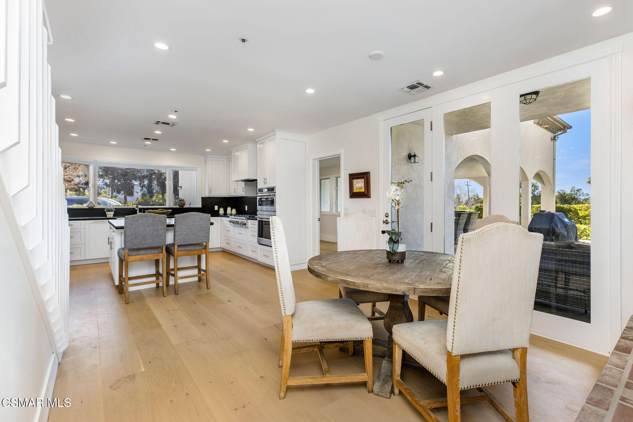 Dining area with a round wood table beside a white kitchen and glass patio doors.