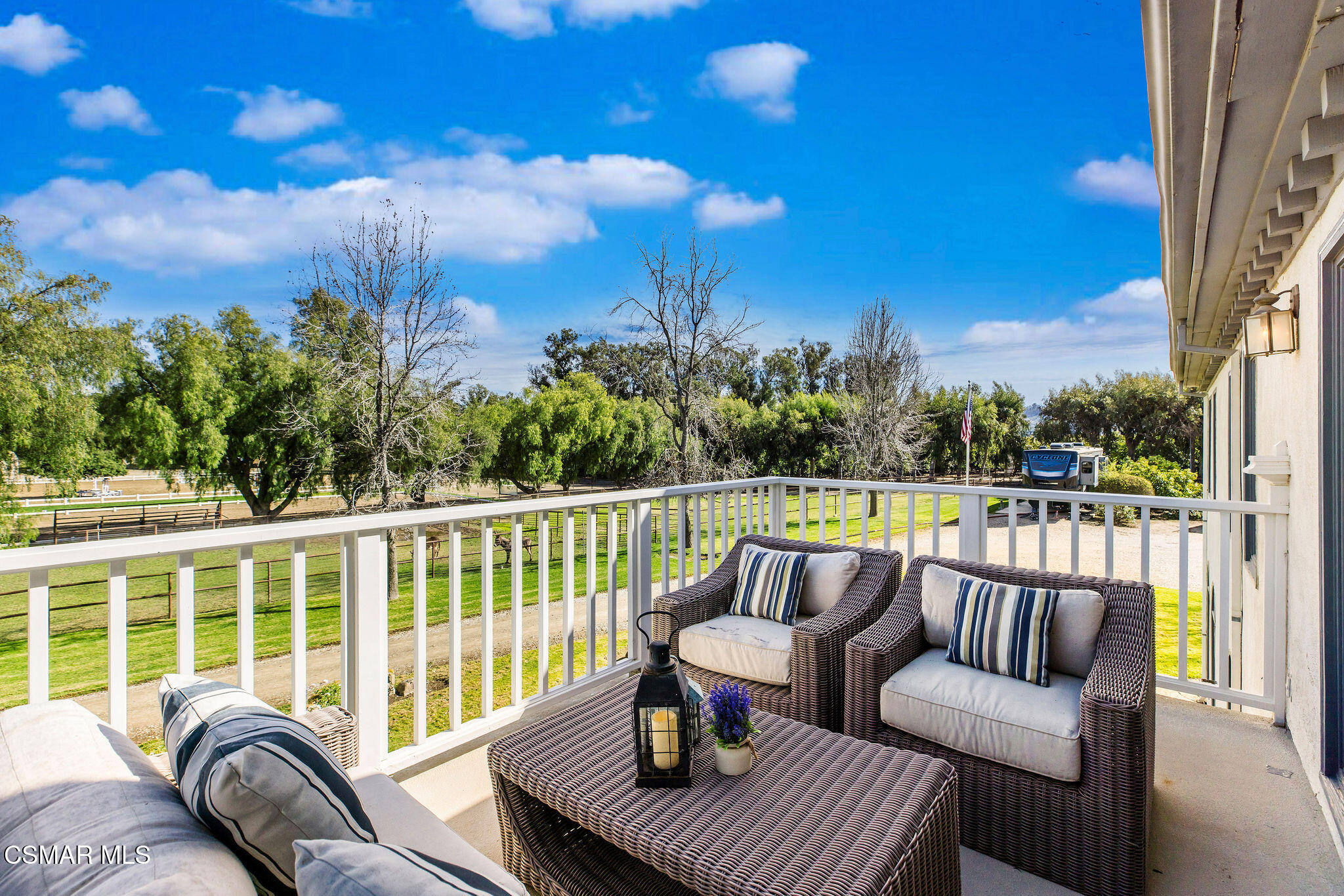 Furnished balcony with wicker seating overlooking a green lawn and mature trees.