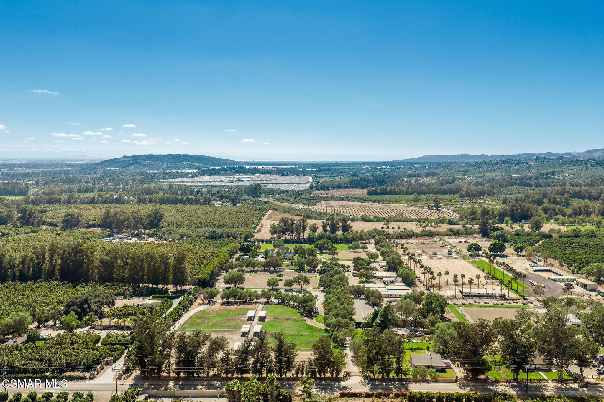 Aerial view of orchards and ranch fields with buildings and rolling hills beyond.