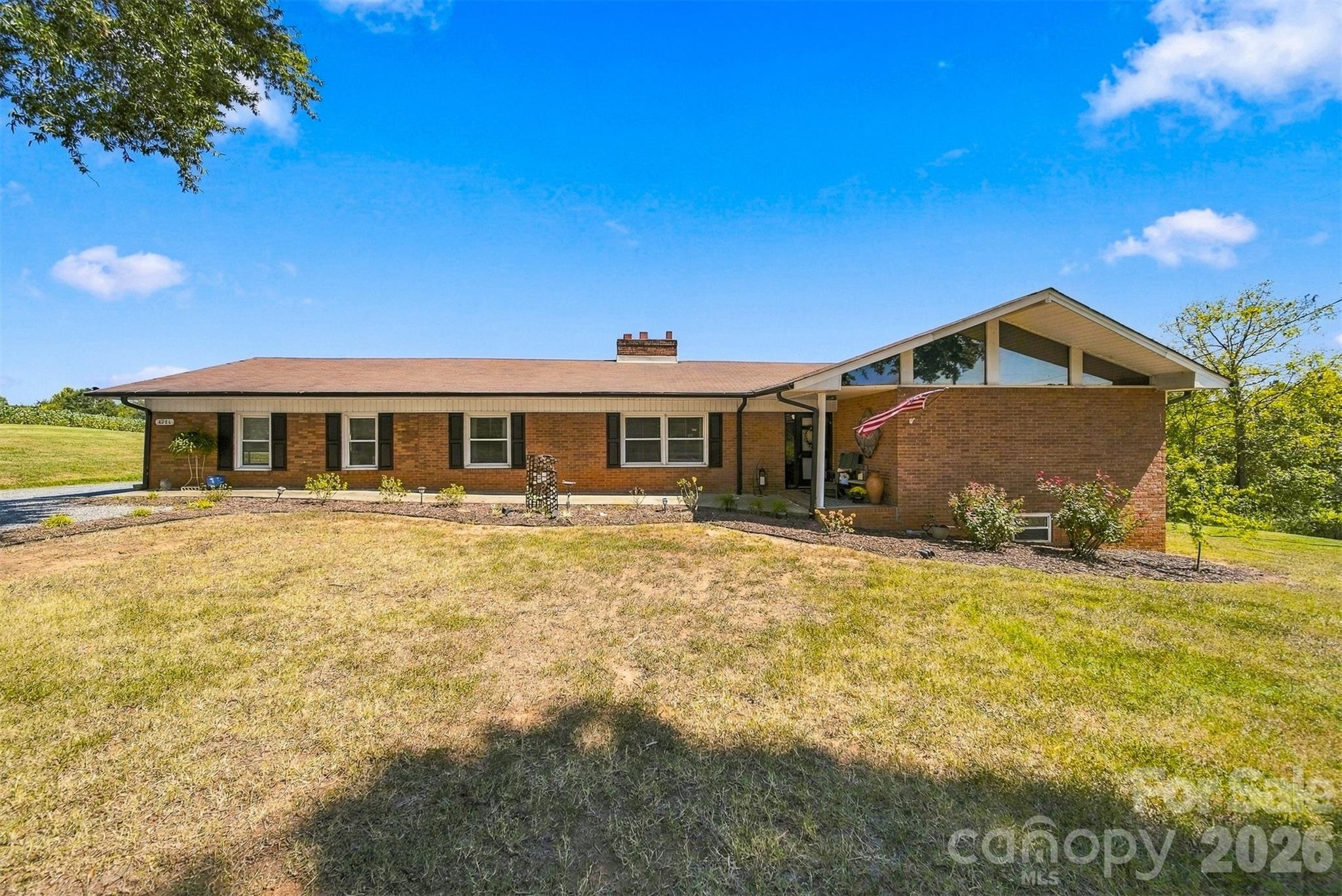 Brick ranch house with a broad gabled roof, triangular windows, and an American flag by the entry.