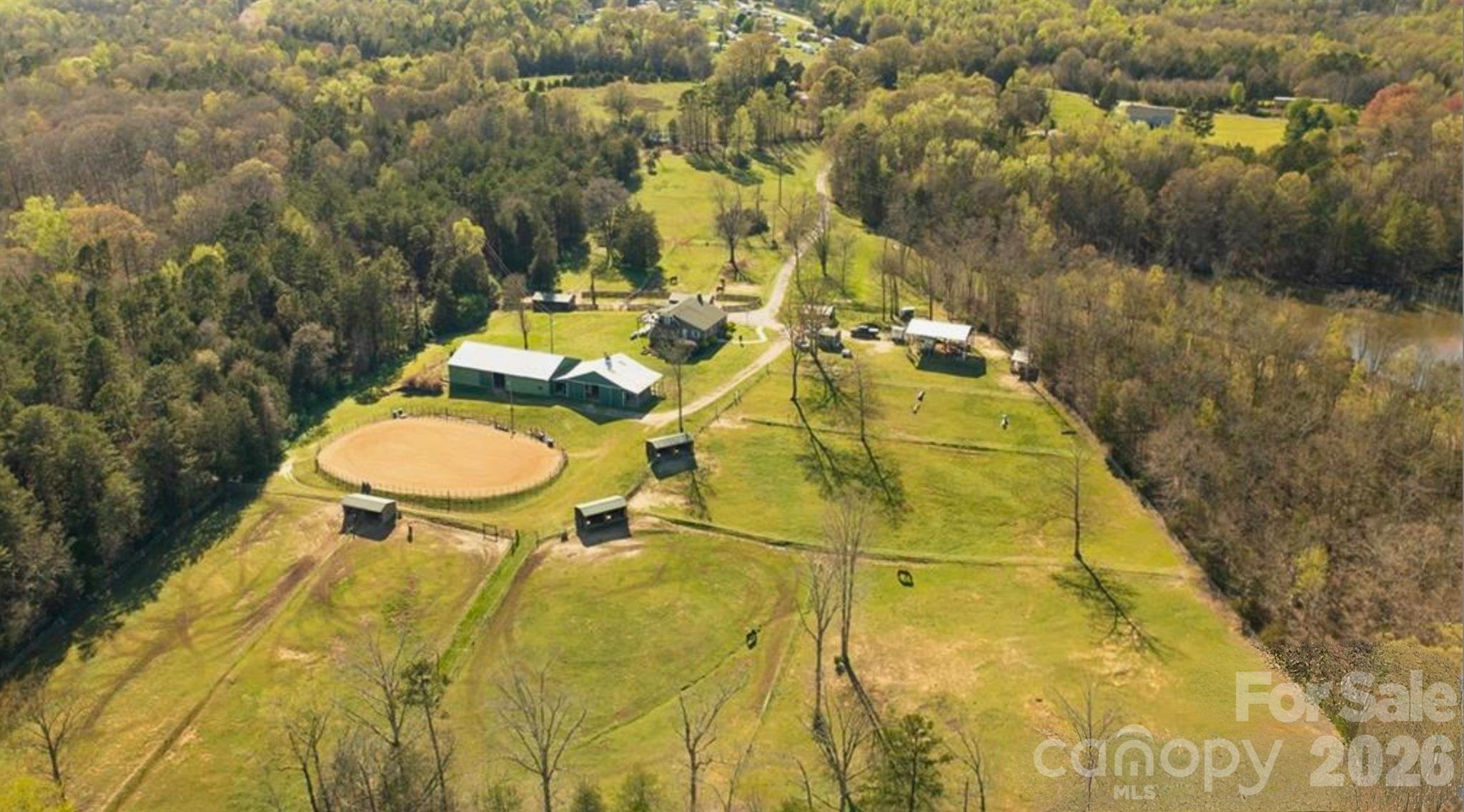 Rural property with fenced pasture, a circular riding area, house, and outbuildings, viewed from above.