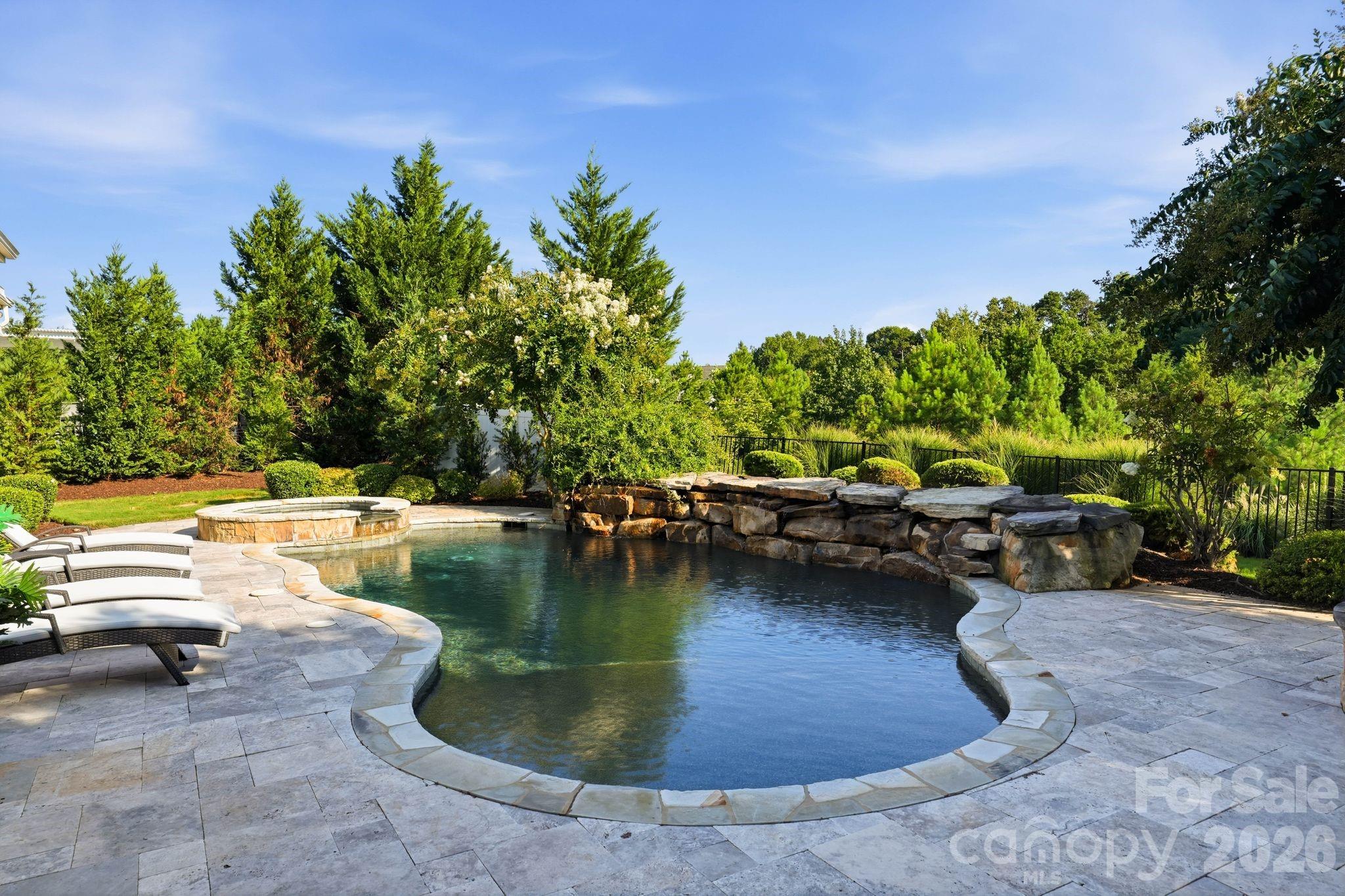 Backyard swimming pool with raised spa, stone wall, and lounge chairs.