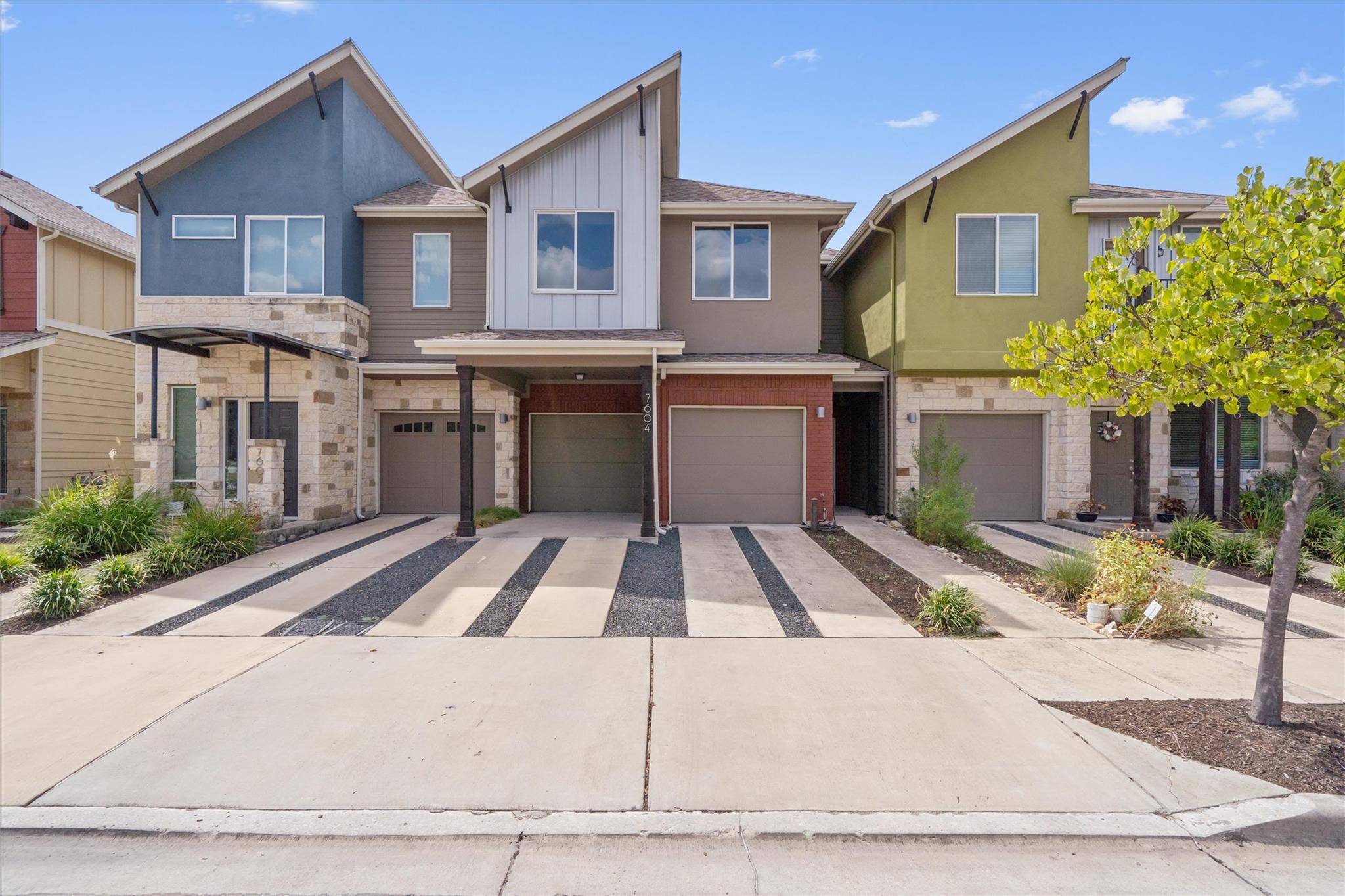 Multistory townhouse with varied-color gables, stone facade, striped driveway, and landscaped frontage.