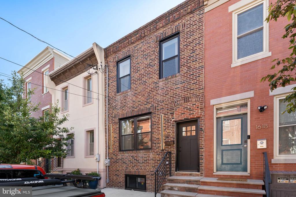 Brick rowhouse with a dark front door, black-framed windows, and front steps.