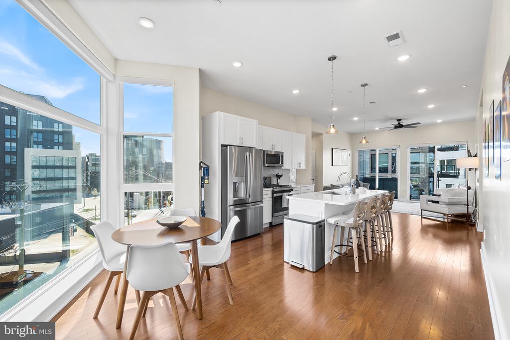 Open-plan condo kitchen and dining area with an island, hardwood floors, and large city-facing windows.