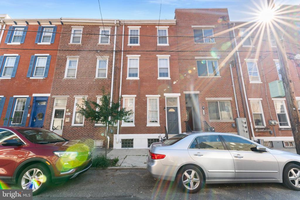 Red-brick rowhouses with white-trimmed windows and a dark front door along a sunny street.
