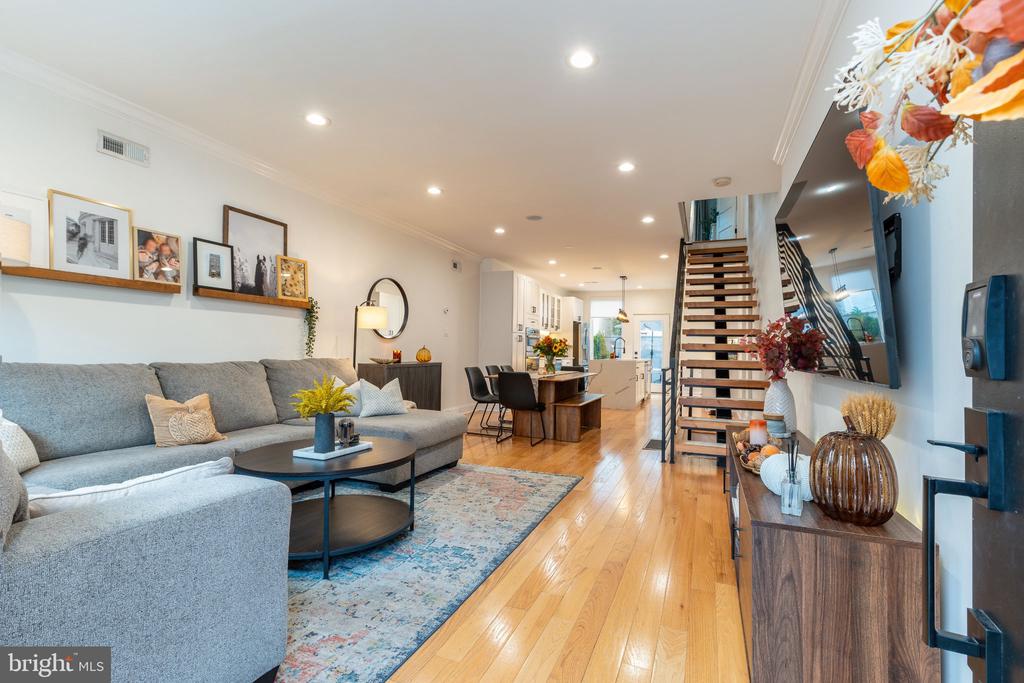 Open-plan living room with a gray sectional, hardwood floors, and an open-riser staircase.