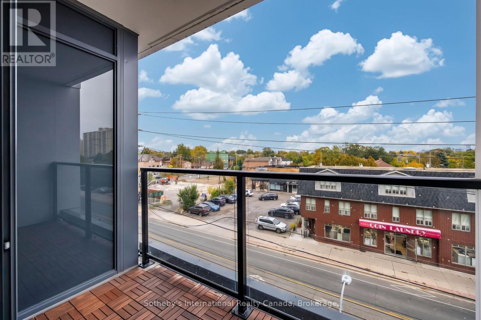 Condo balcony overlooking a neighborhood street, with wood-look deck tiles and a glass railing.