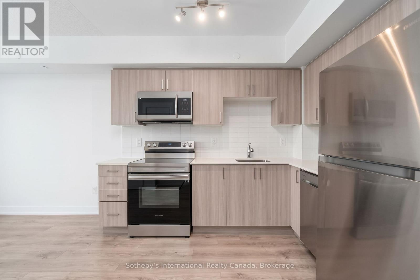 Modern kitchen with light wood cabinets, stainless steel appliances, and pale wood-look flooring.