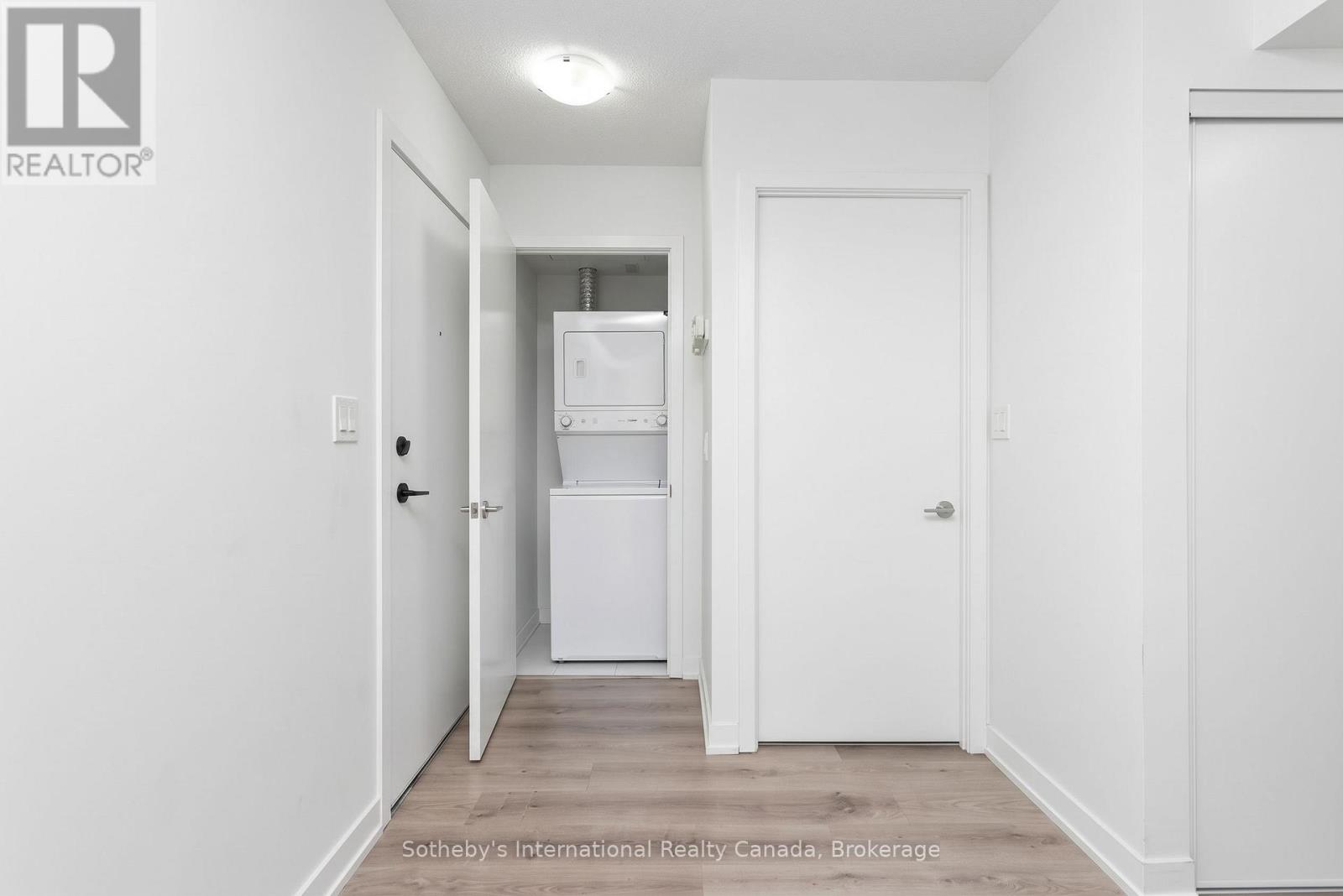 Condo hallway with an open laundry closet showing a stacked washer and dryer.