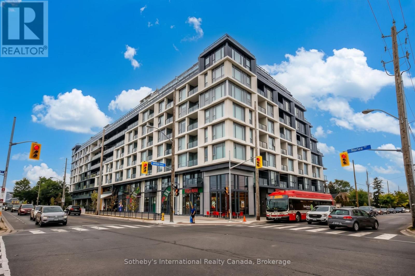 Modern condominium building with glass balconies and ground-floor shops at a busy intersection.