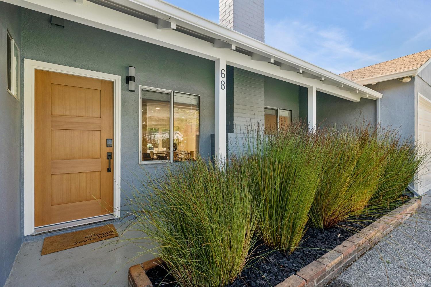 Home entrance with a wood door, gray-blue siding, and ornamental grasses along the walkway.