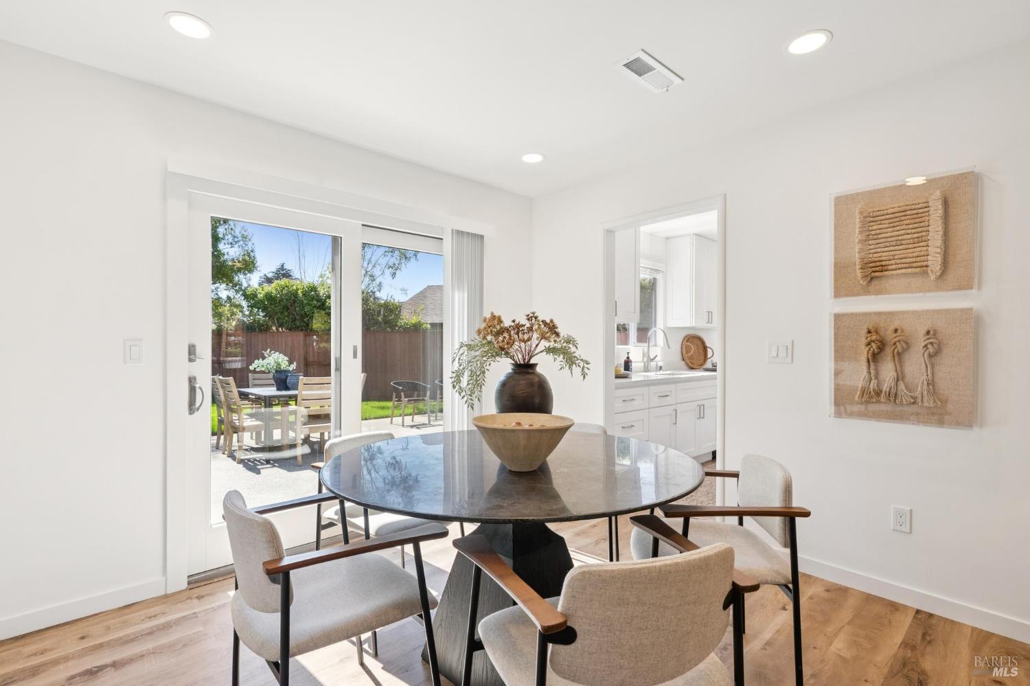 Dining area with a round table, sliding doors to a sunny patio, and an adjoining white kitchen.