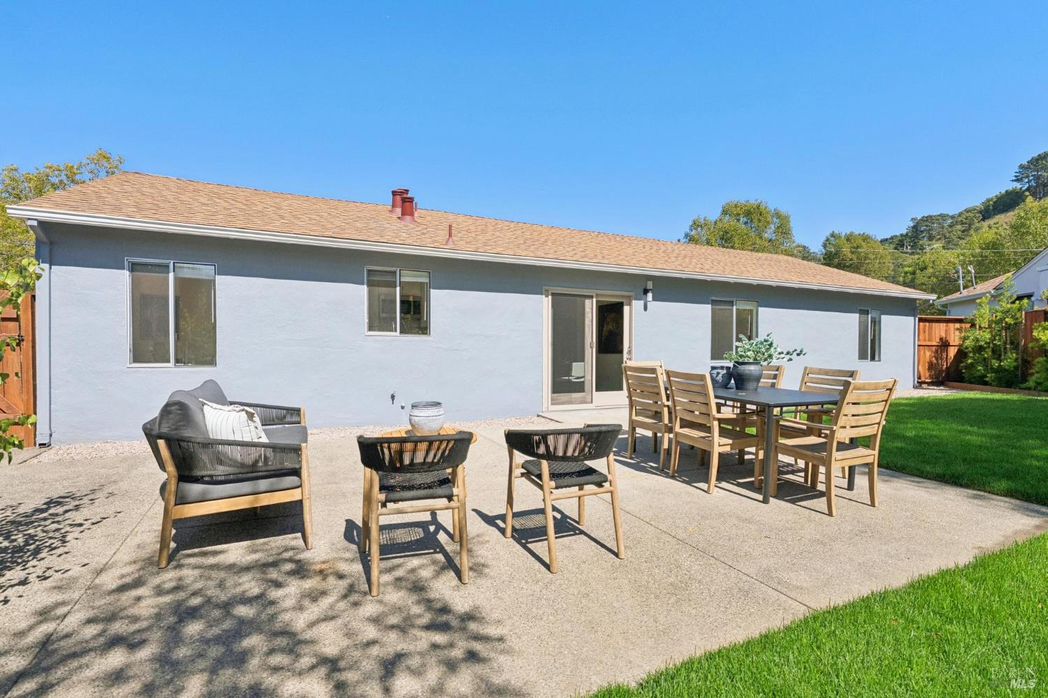 Rear patio with outdoor dining and lounge furniture beside the home and lawn.