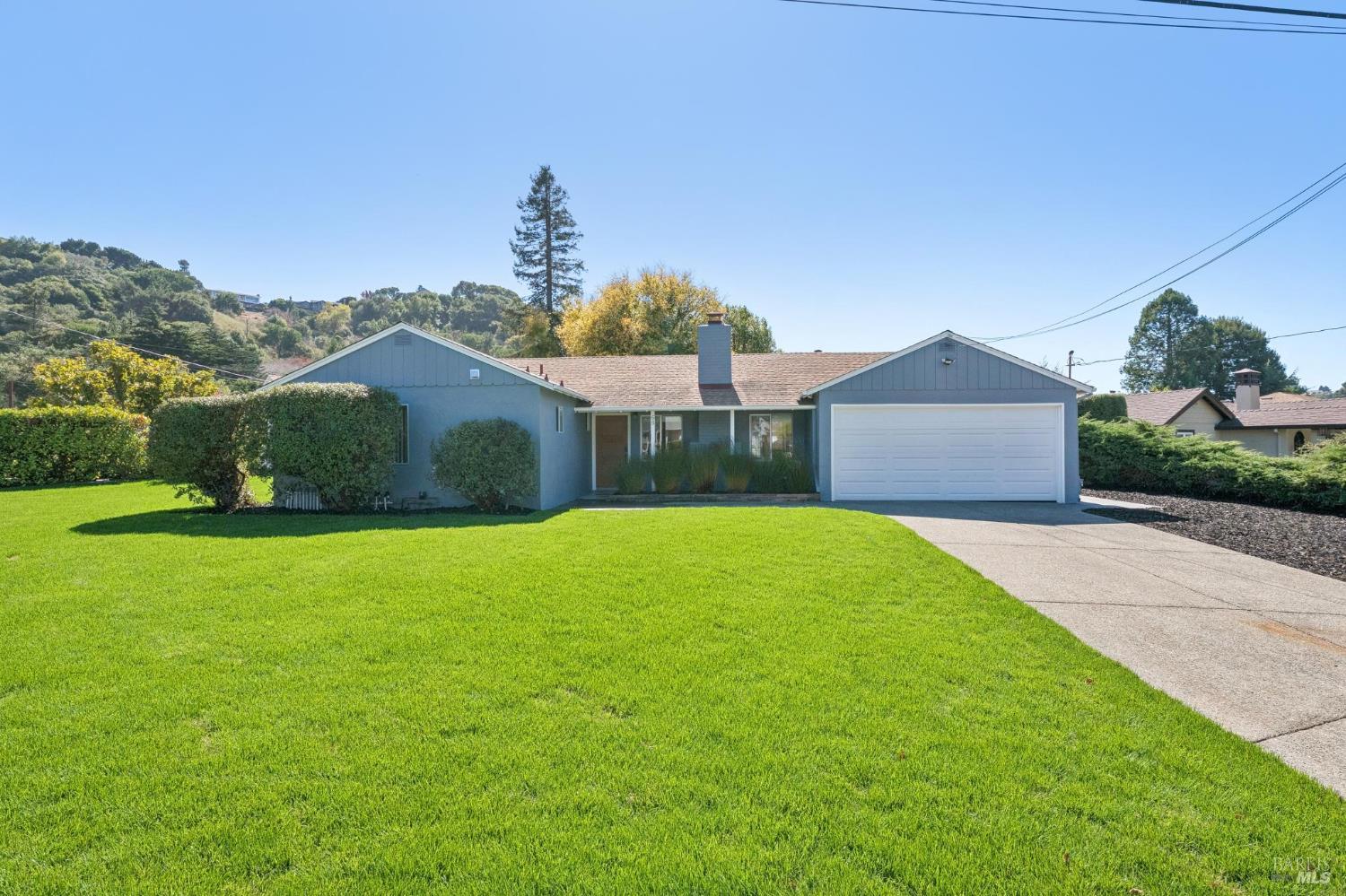 Single-story blue-gray home with a white two-car garage, broad lawn, and concrete driveway.