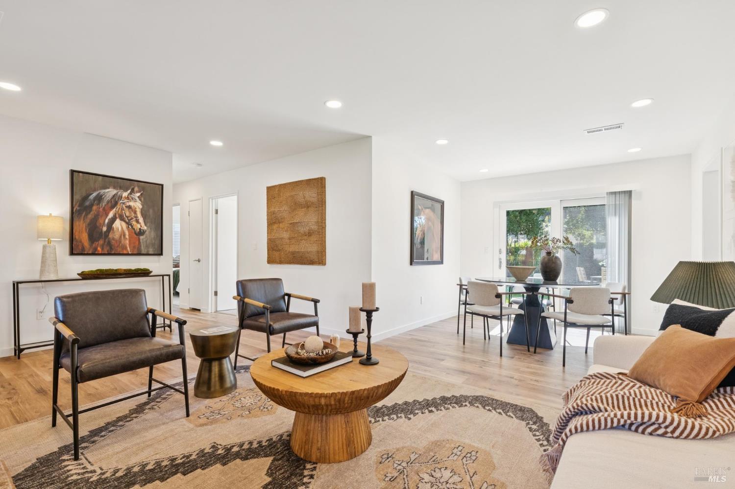 Open-plan living and dining room with leather chairs, a round wood coffee table, and sliding glass doors.