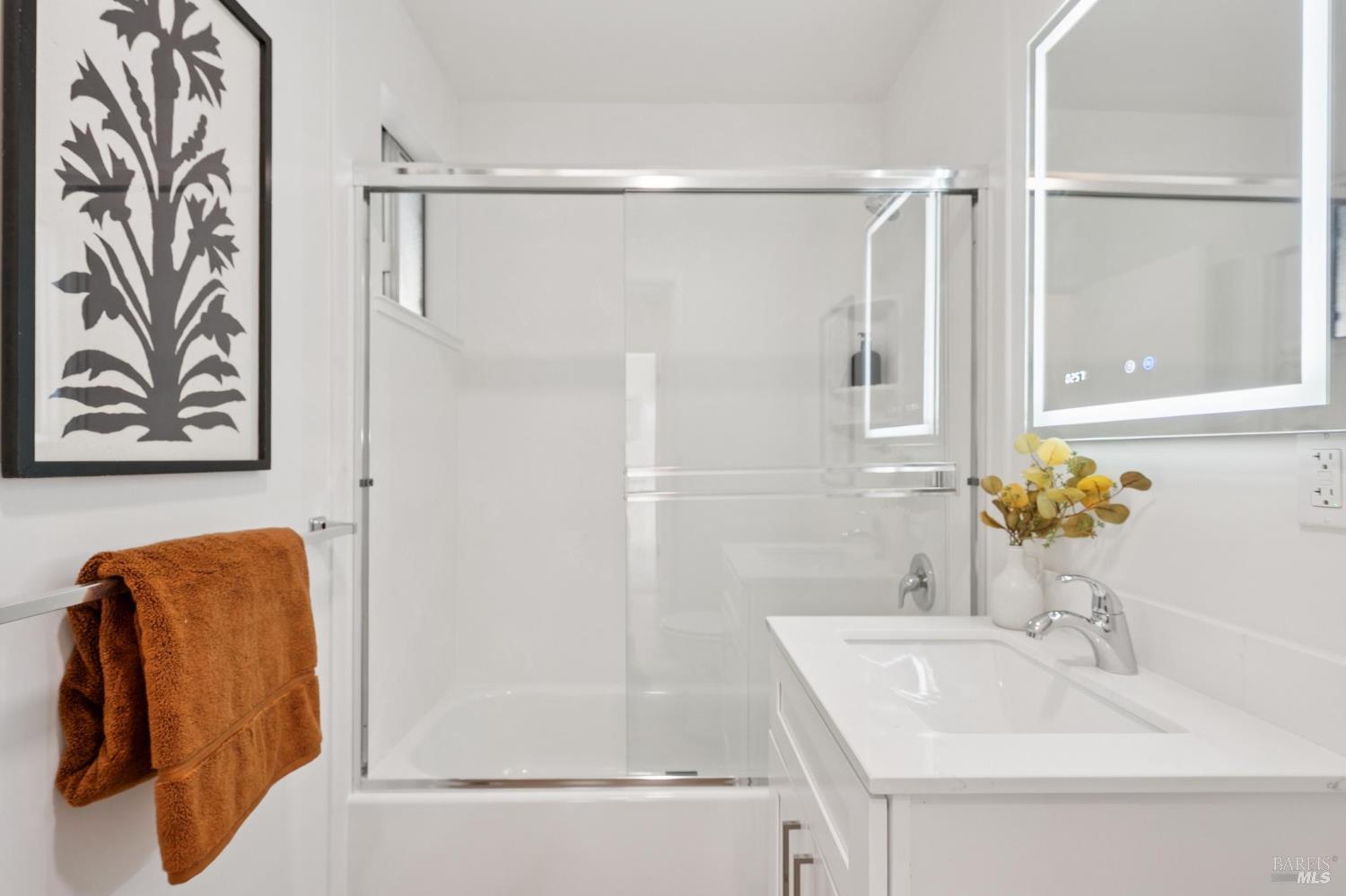 Bright white bathroom with a glass-enclosed shower, vanity, and rust-colored towels.