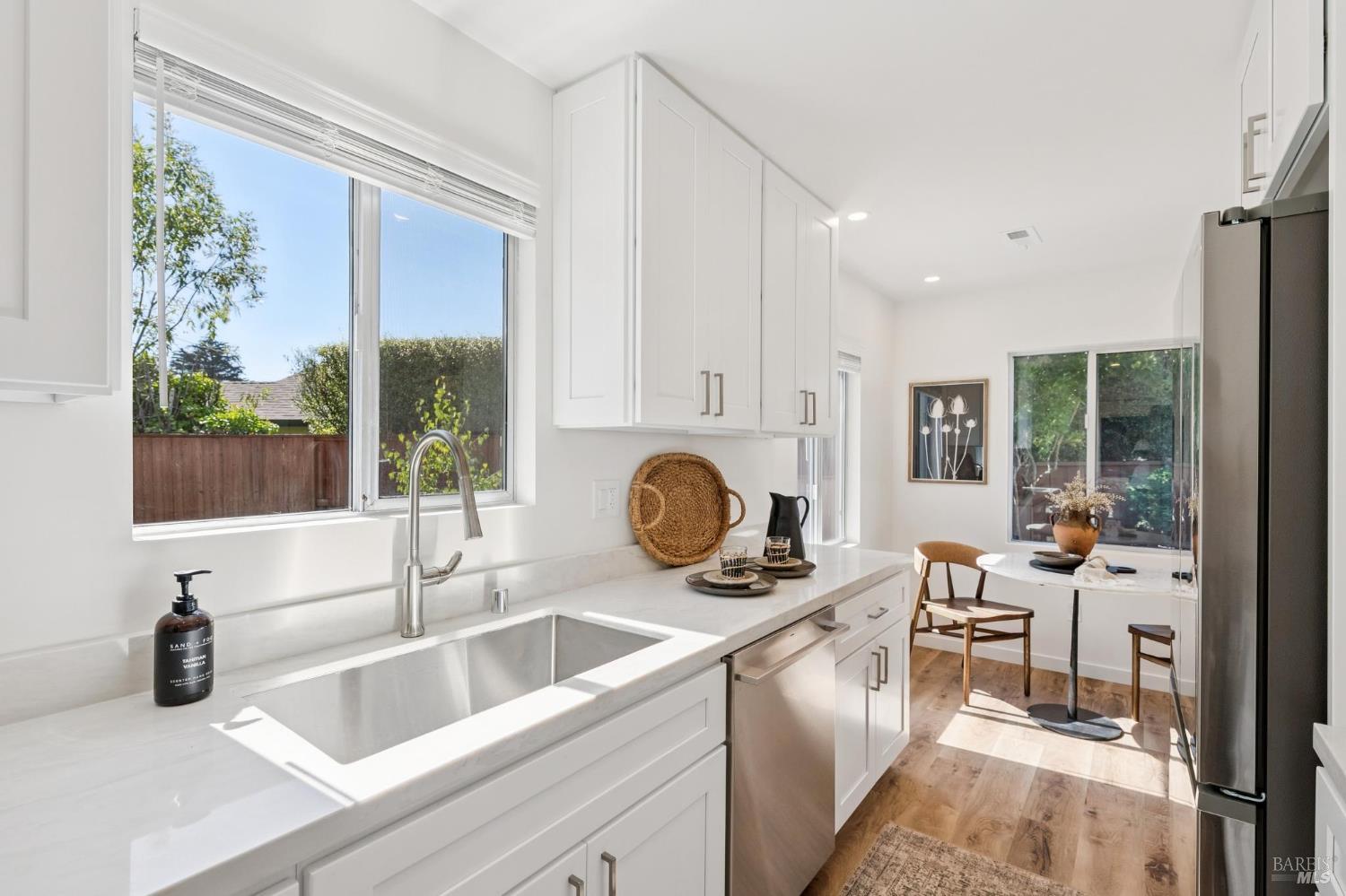 Bright white kitchen with a farmhouse sink, stainless appliances, and a dining nook beside large windows.