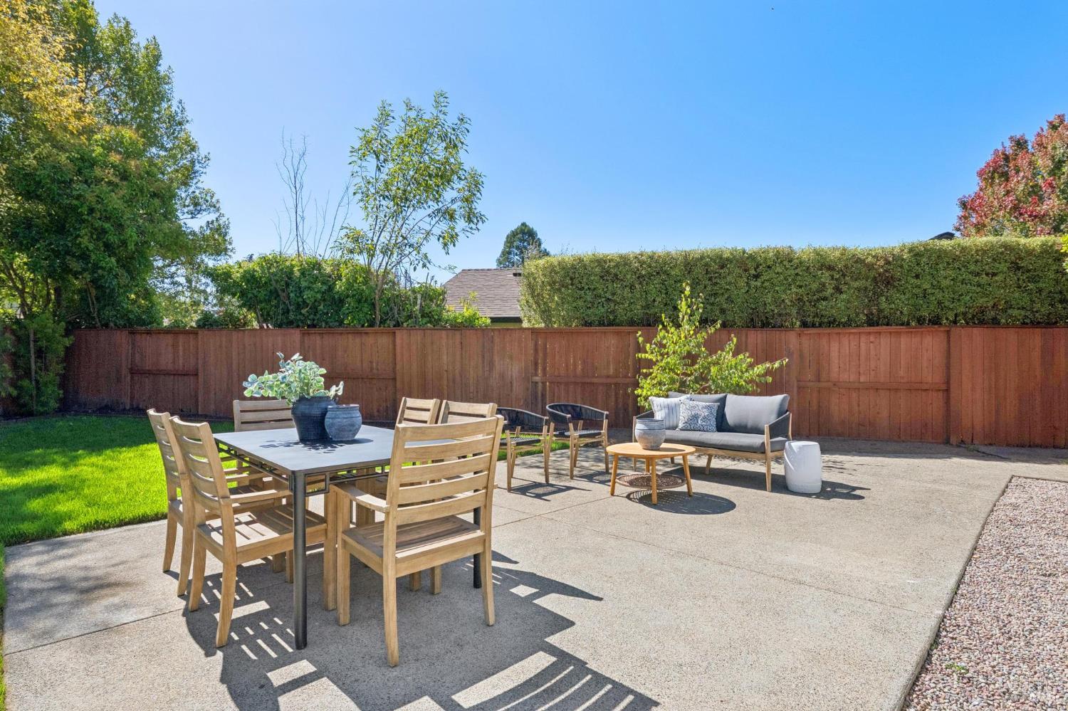 Furnished backyard patio with a dining table, lounge seating, lawn, and wooden privacy fence.