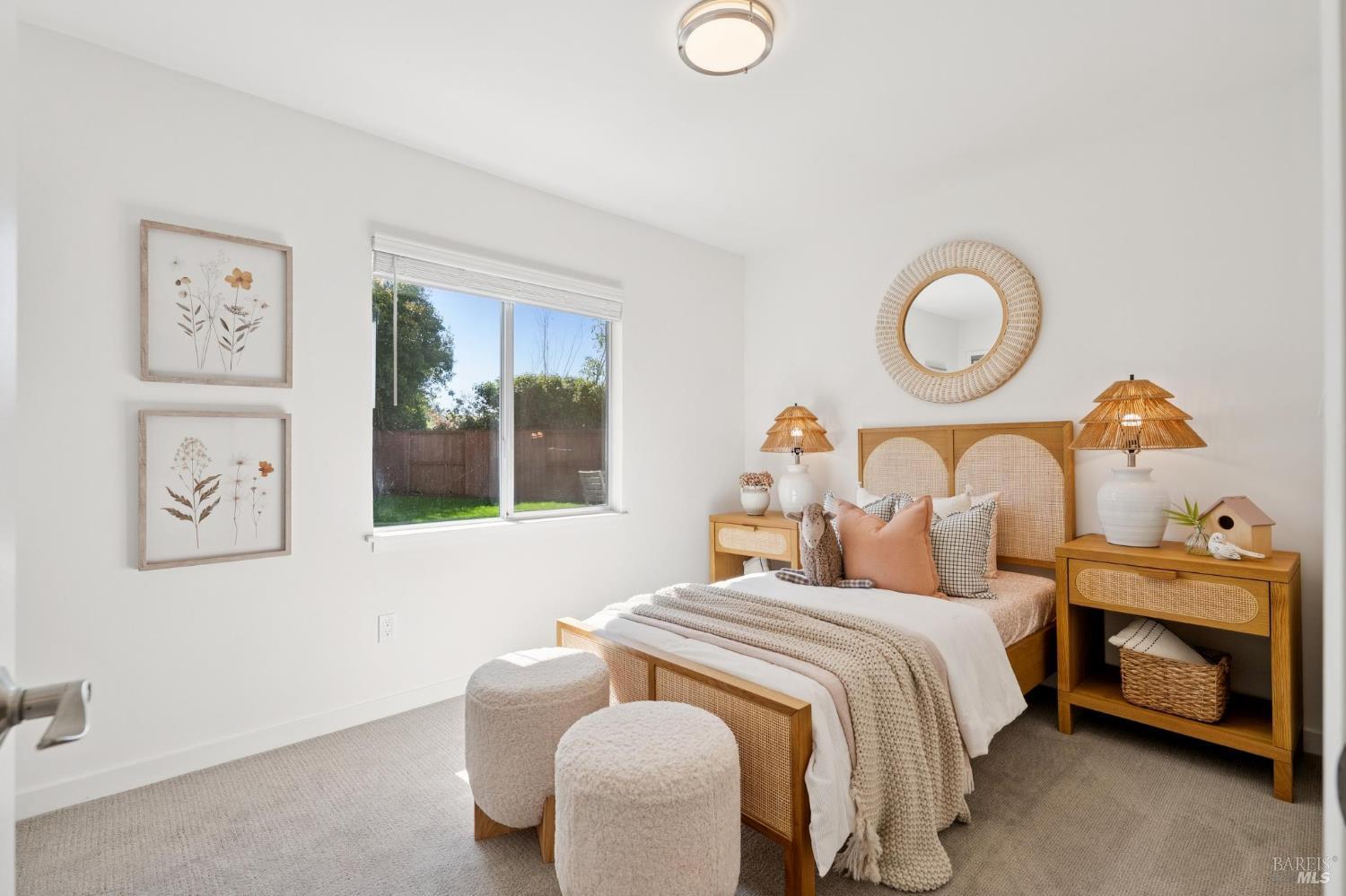 Staged bedroom with a rattan bed, woven accents, and a window overlooking a fenced yard.