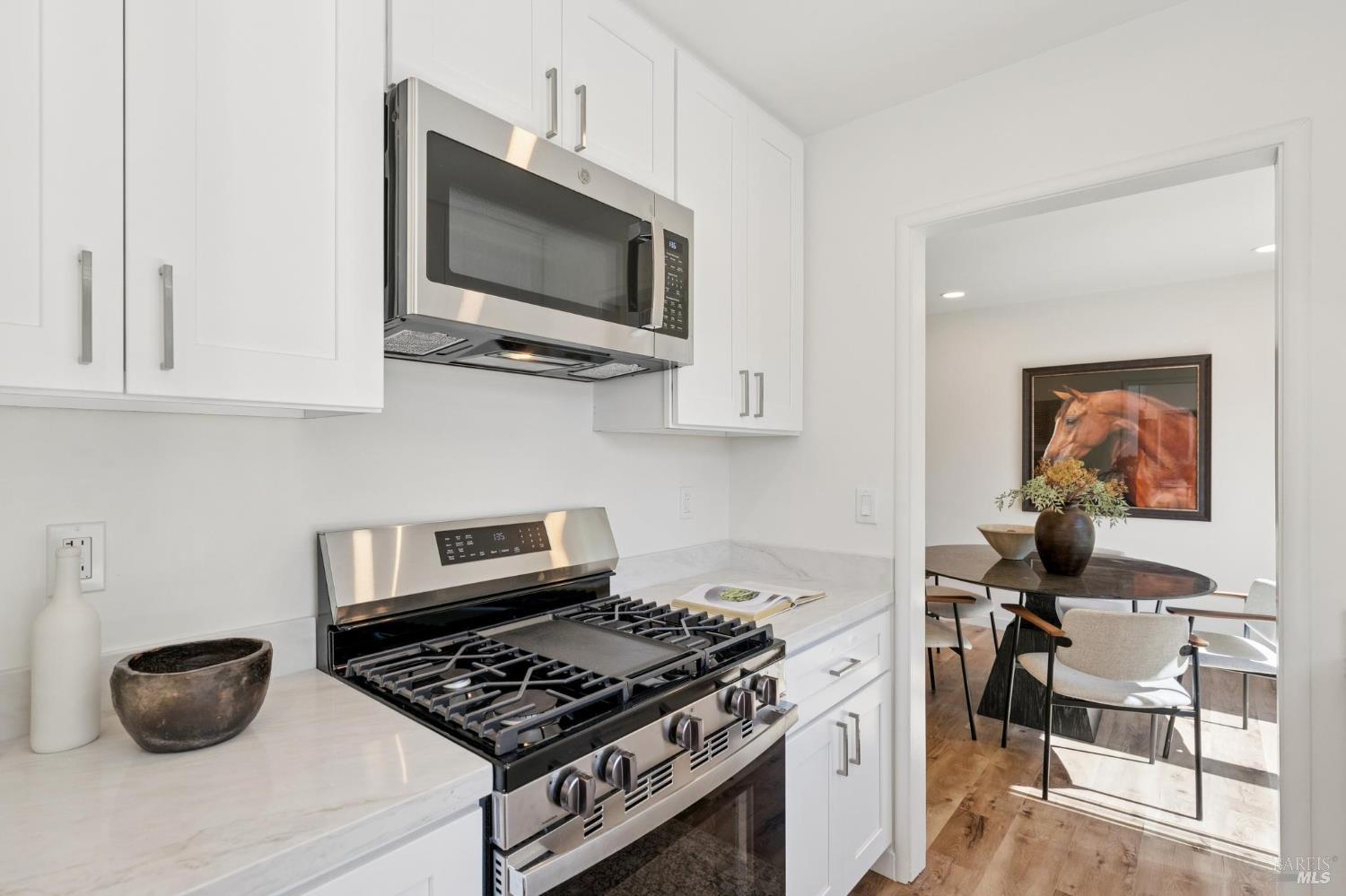 Updated kitchen with white cabinets, stone counters, and stainless-steel gas range beside a dining area.