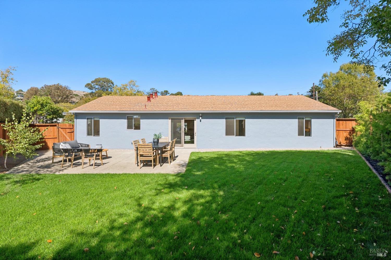 Rear of a single-story blue house with a furnished patio and broad green lawn.