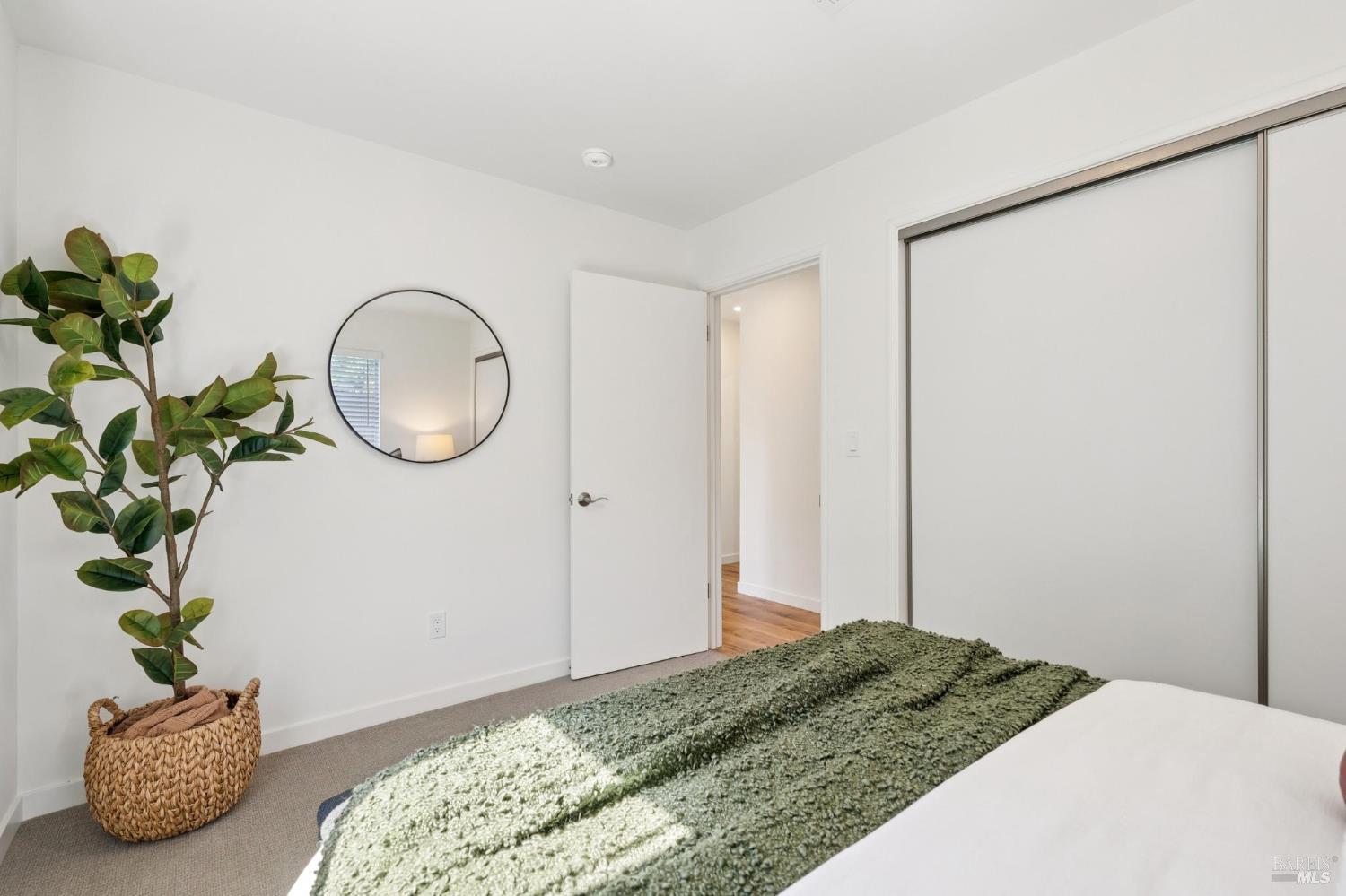 Bedroom with a textured green bedspread, sliding closet doors, and a potted plant.
