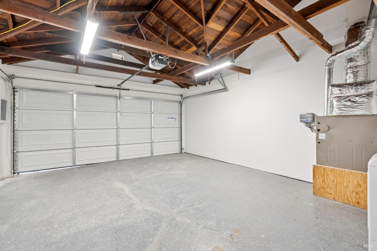 Empty garage with exposed timber rafters, a concrete floor, and a wide sectional door.
