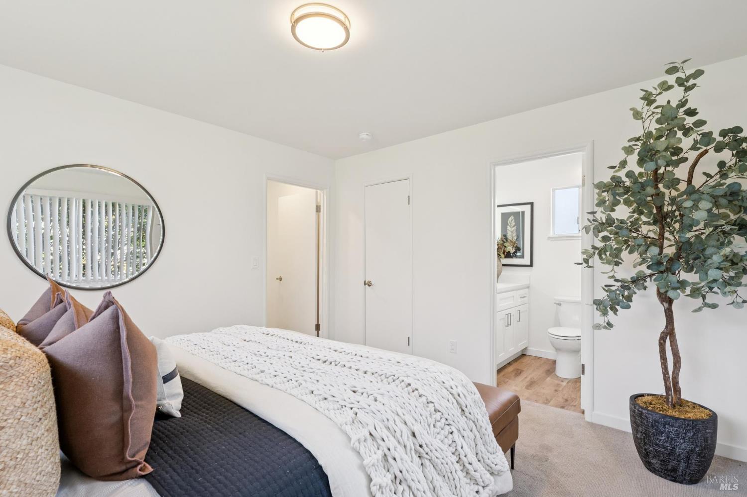 Furnished bedroom with a chunky white knit blanket, oval mirror, and adjoining bathroom.