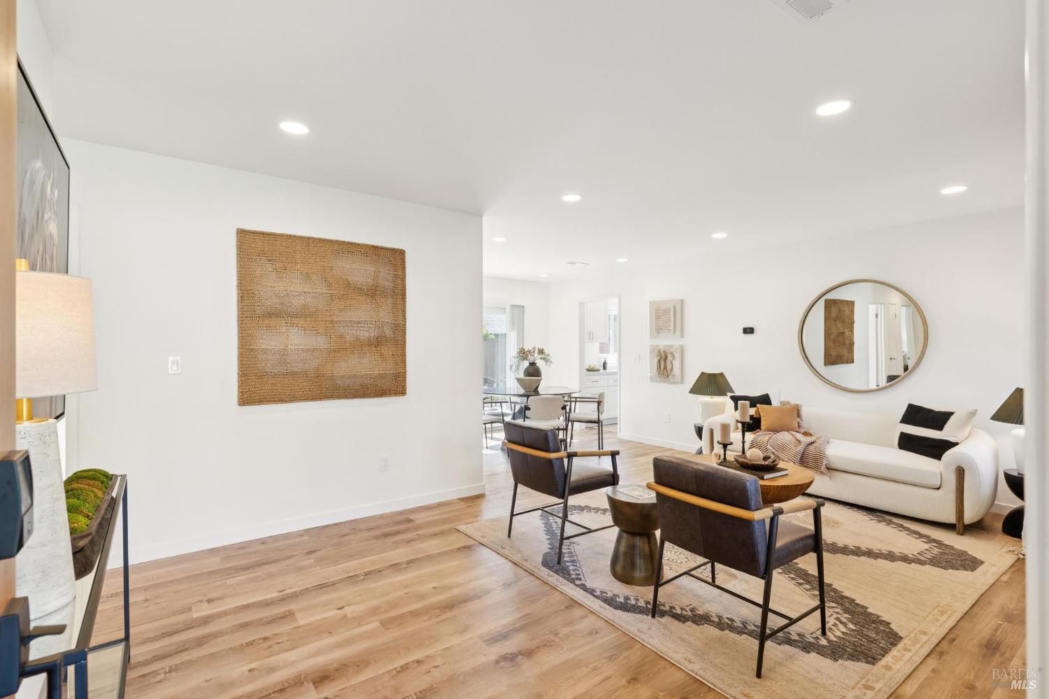 Living room with white sofa, wood floors, patterned rug, and open dining area.