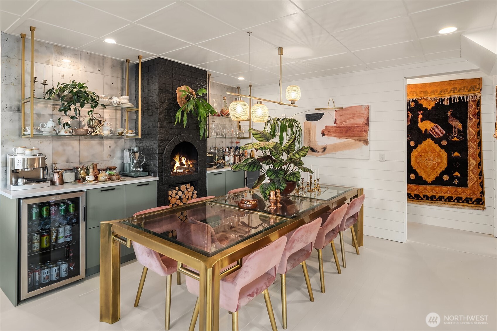 Dining area with a brass-framed glass table, pink chairs, and a black brick fireplace.