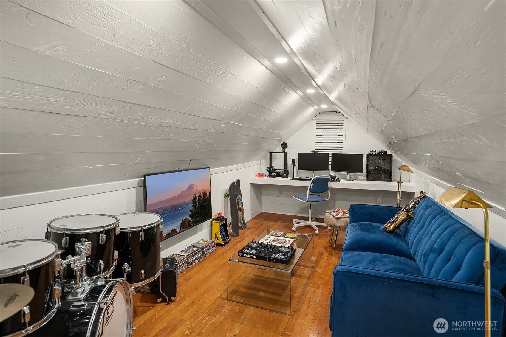 Finished attic bonus room with a blue sofa, desk, drum kit, and music equipment.