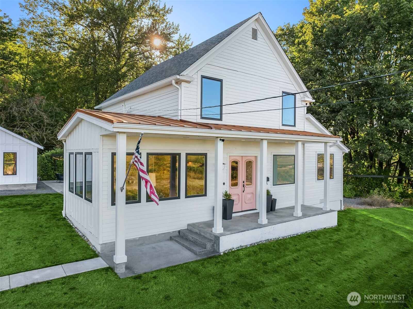 White two-story farmhouse with pink double doors, a copper porch roof, and a green lawn.