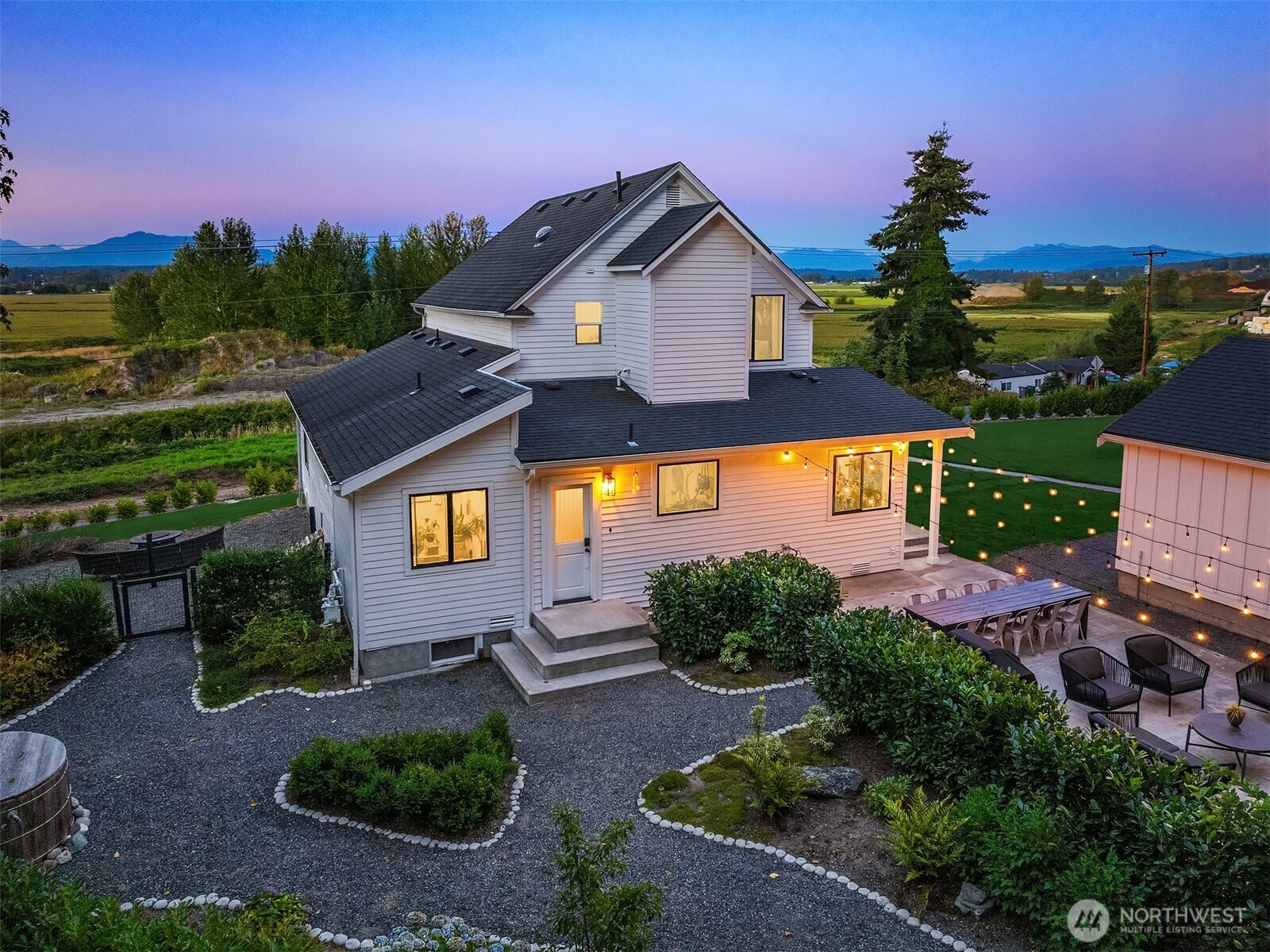 White two-story home with a string-lit patio, landscaped gravel yard, and distant mountain views at dusk.