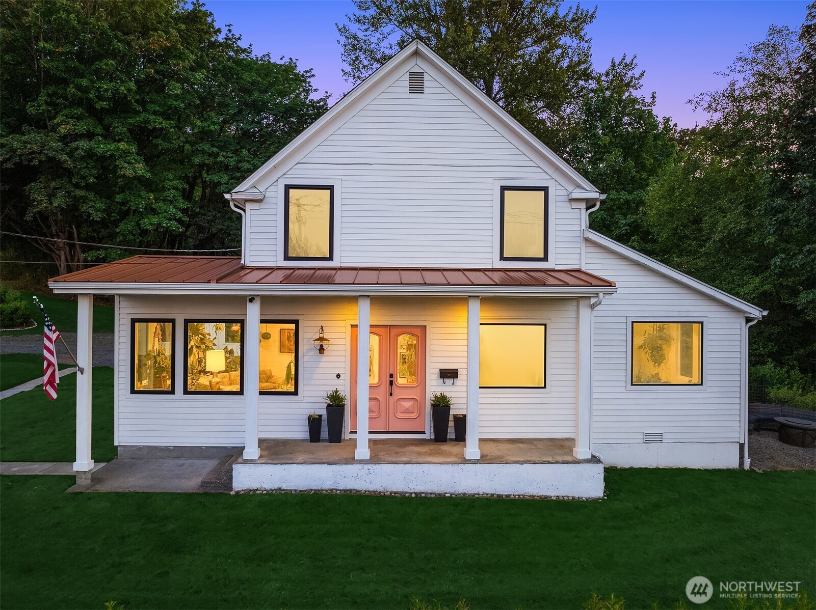 White two-story house with a copper-colored porch roof and pink double doors at dusk.