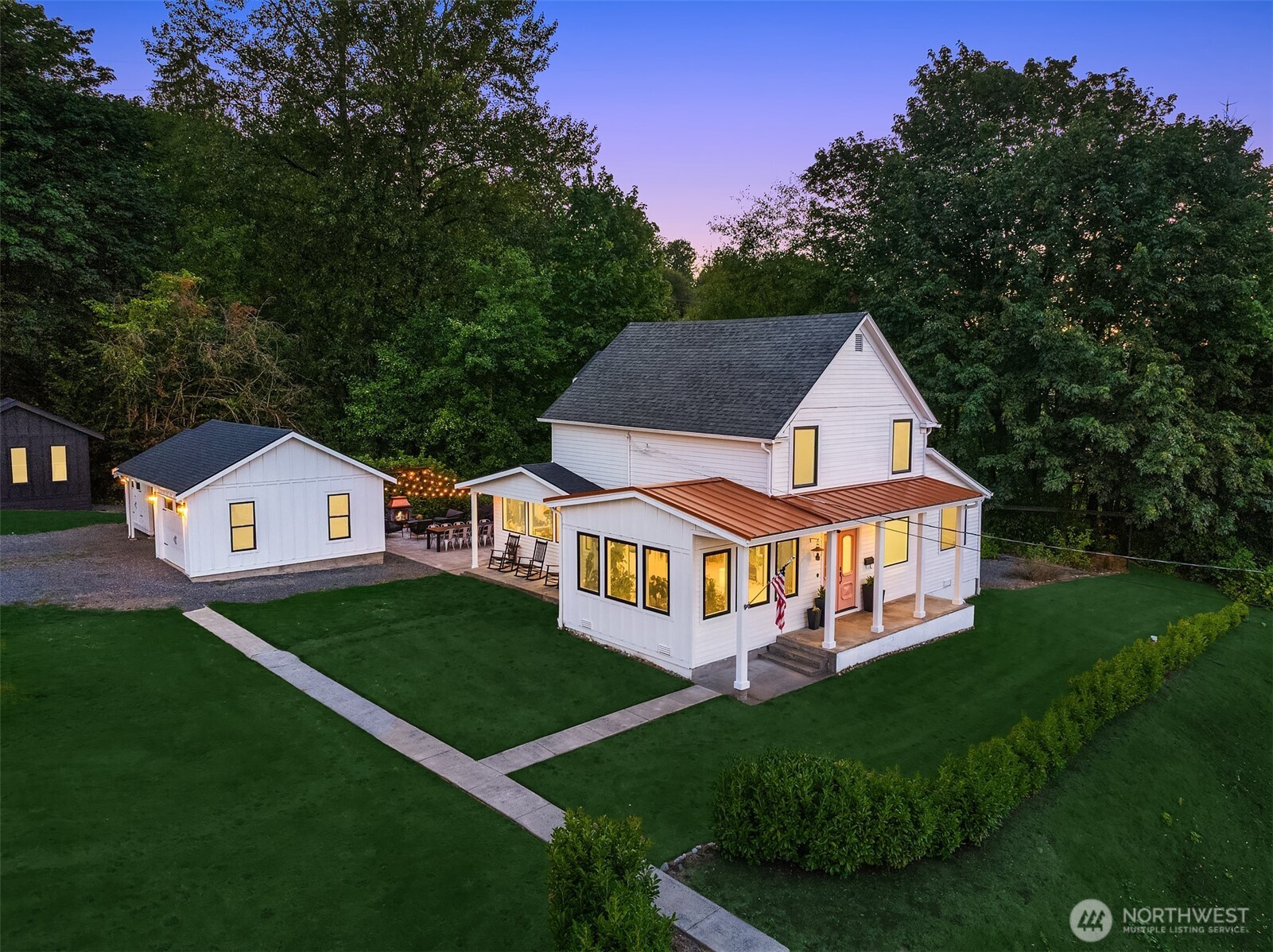 White two-story home with a covered porch, detached outbuilding, and broad lawn at dusk.