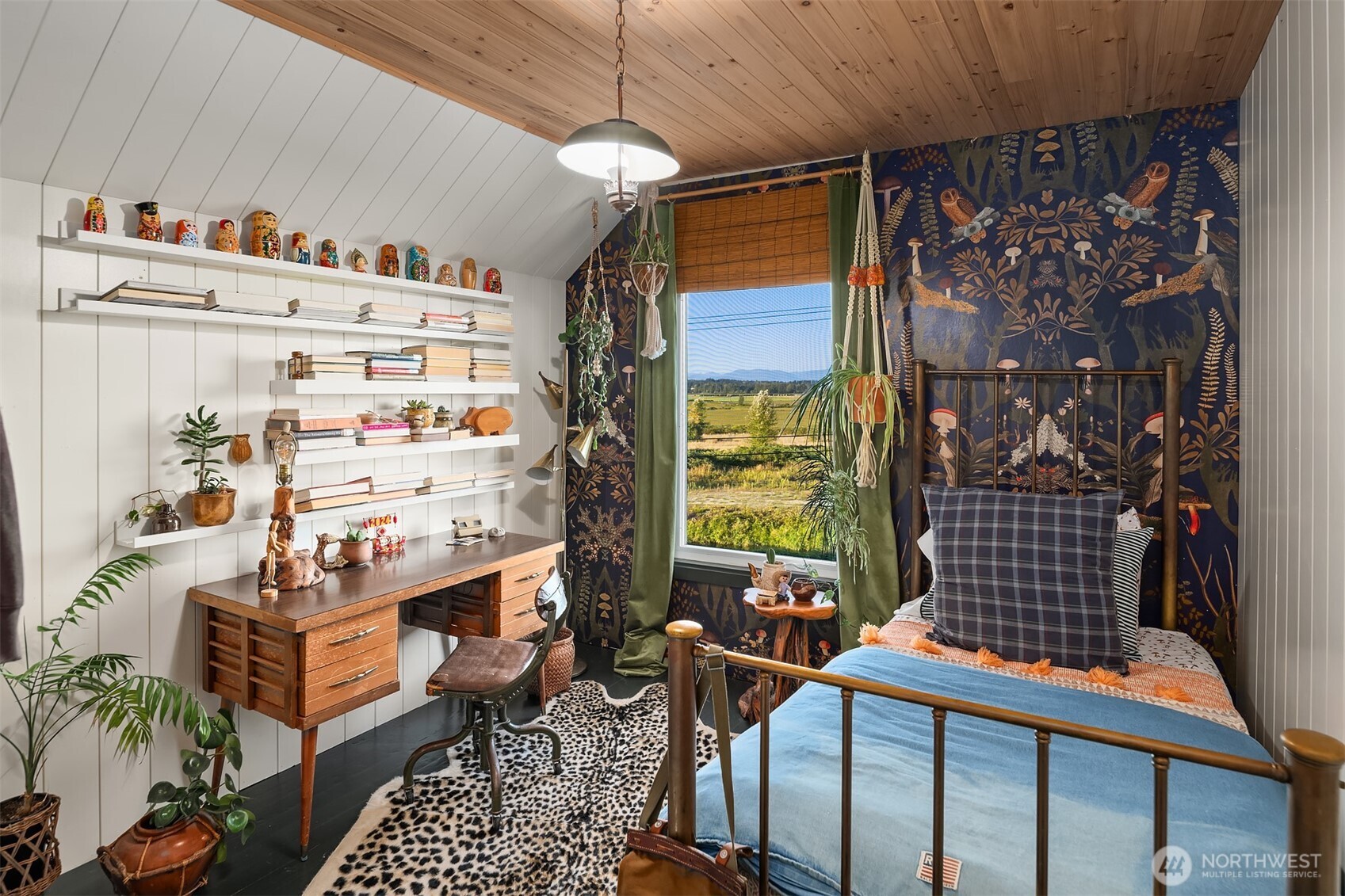 Bedroom with a sloped wood ceiling, patterned wallpaper, and a window overlooking fields.