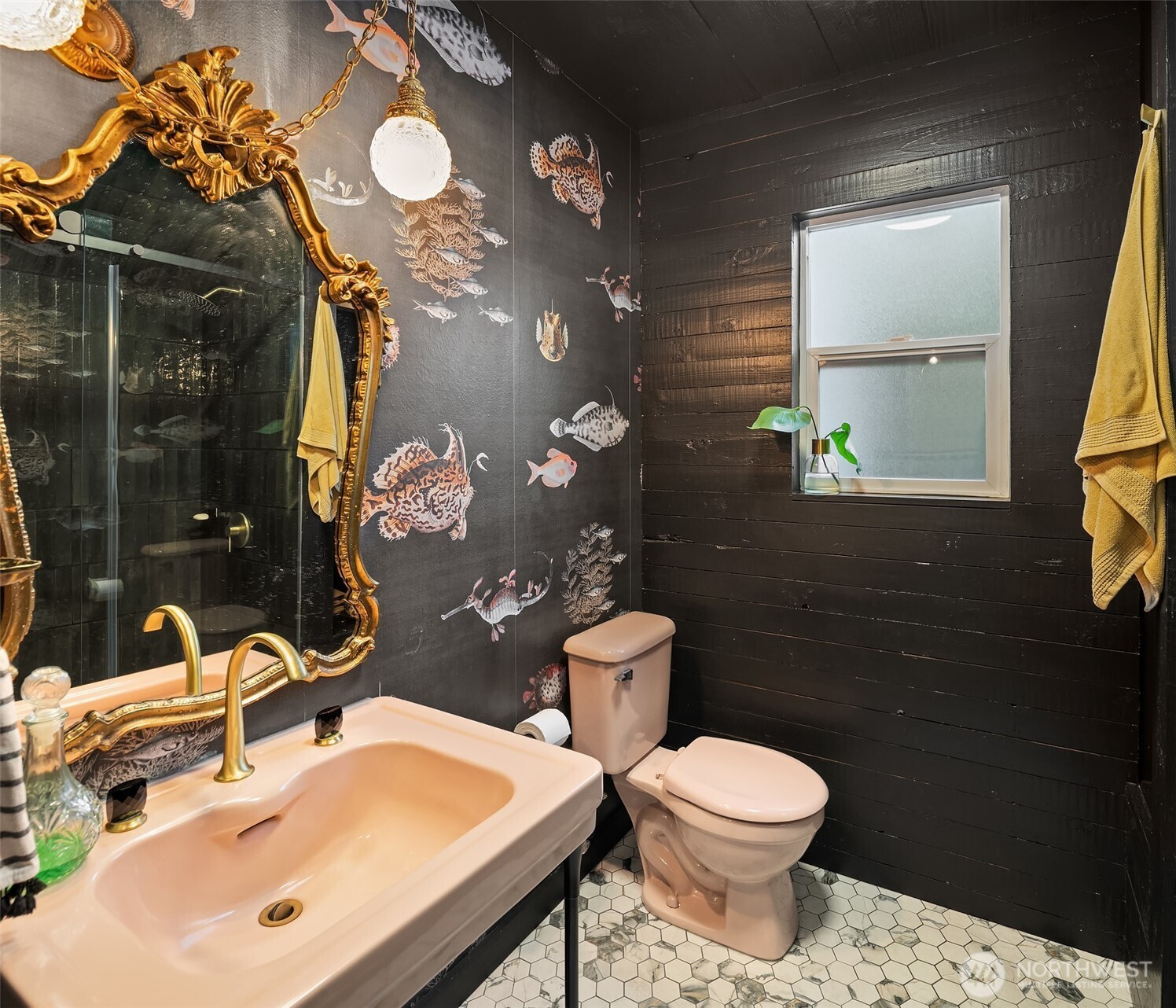 Bathroom with fish-patterned wallpaper, black wood walls, and a large ornate gold mirror.