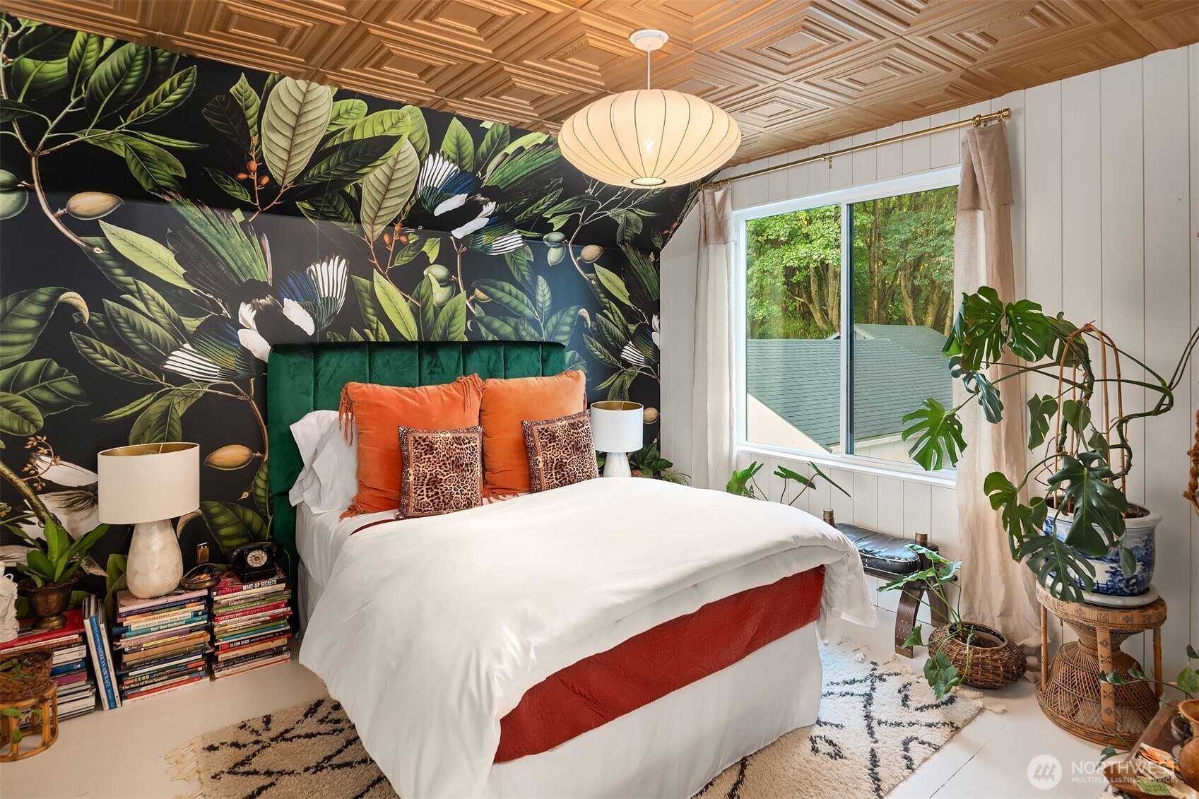 Bedroom with tropical-leaf wallpaper, a green headboard, orange pillows, and a carved wood ceiling.