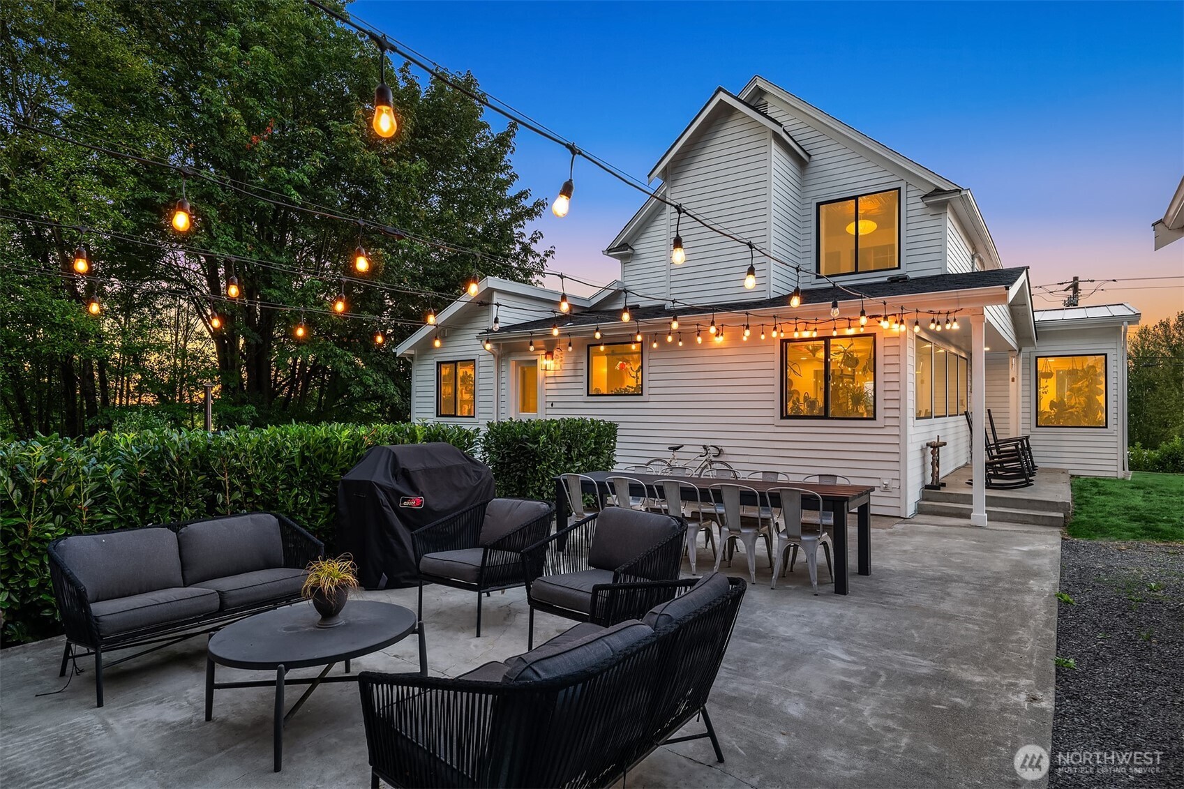 White two-story home with a furnished patio and glowing string lights at dusk.