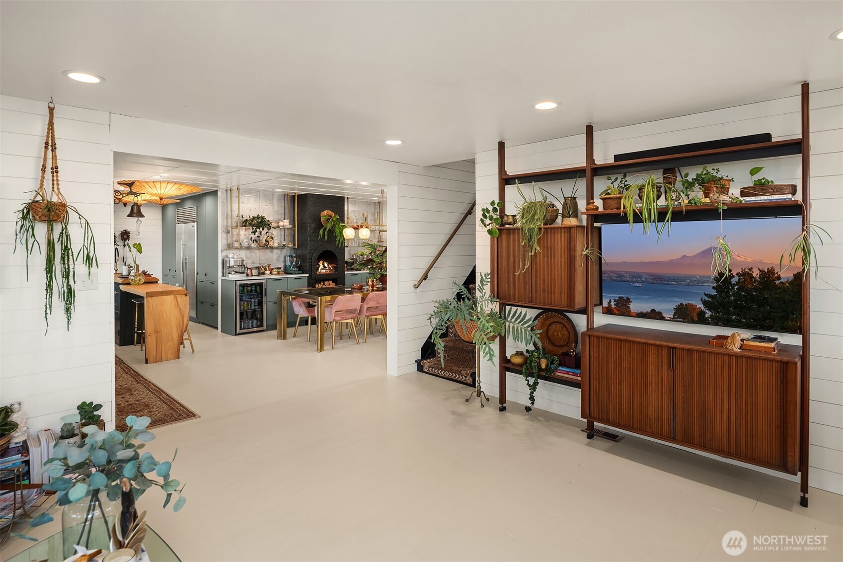 Open-plan living room and kitchen with a wood island, fireplace, and walnut shelving around a large television.