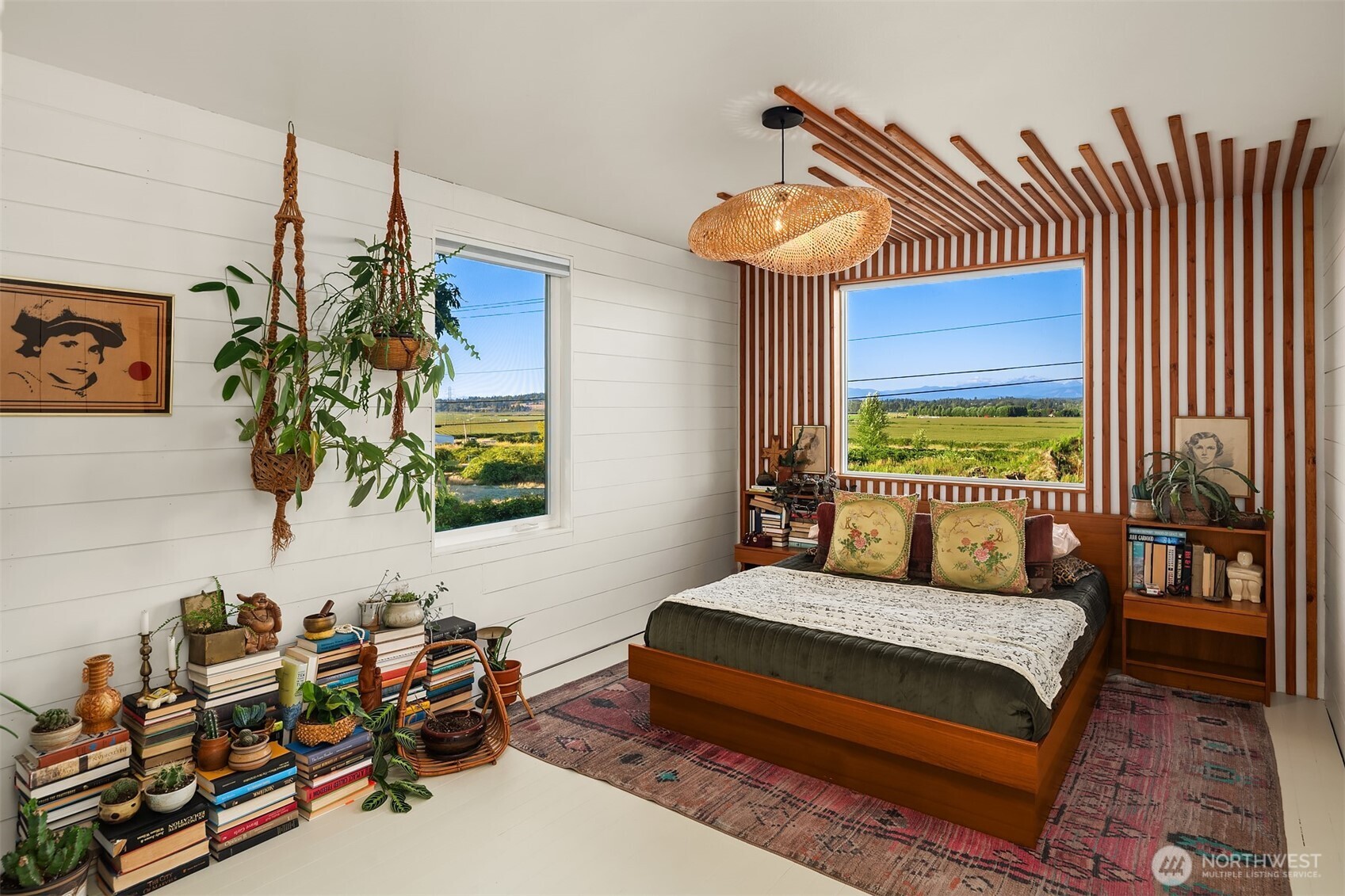 Bedroom with a wood-slat accent wall, woven pendant light, and a window overlooking fields and distant mountains.