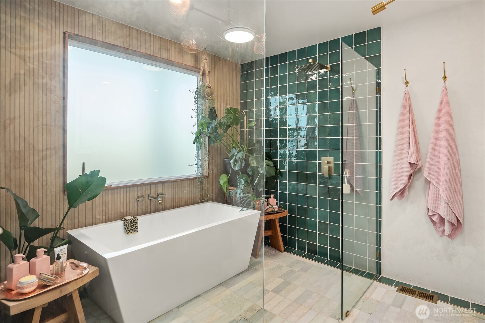 Bathroom with a freestanding tub, green tiled shower, brass fixtures, and wood-look wall paneling.