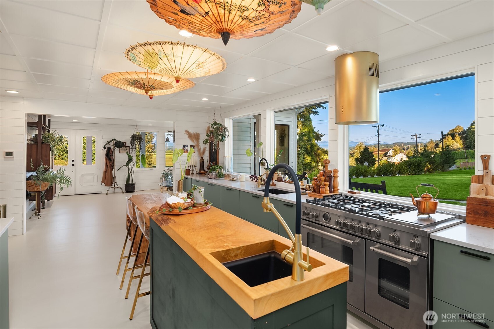 Kitchen with green cabinets, a wood-topped island, stainless steel range, and large windows overlooking the lawn.