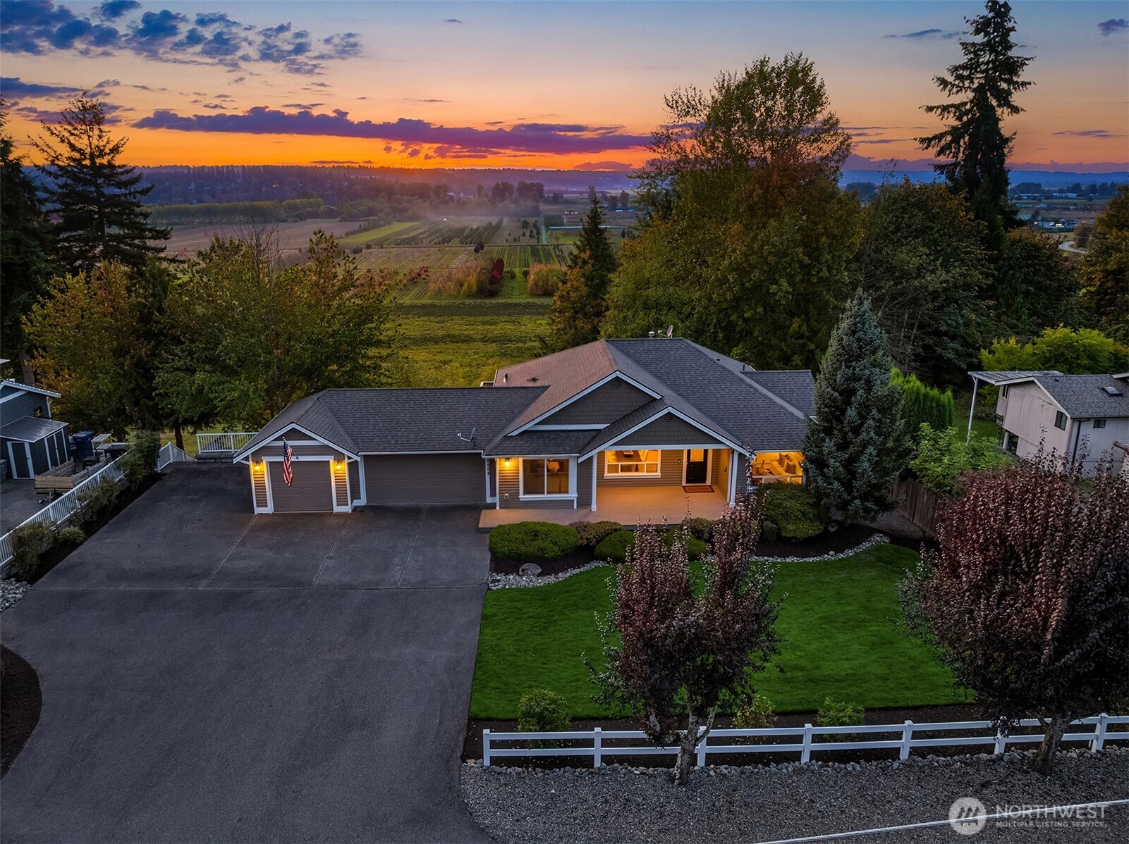Single-story home and landscaped yard at dusk, with orchard fields visible beyond the property.