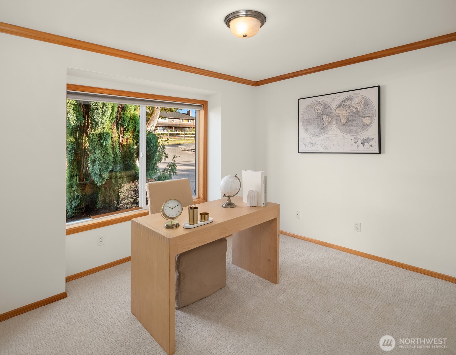Home office with a light wood desk, beige carpet, and a large window overlooking trees.