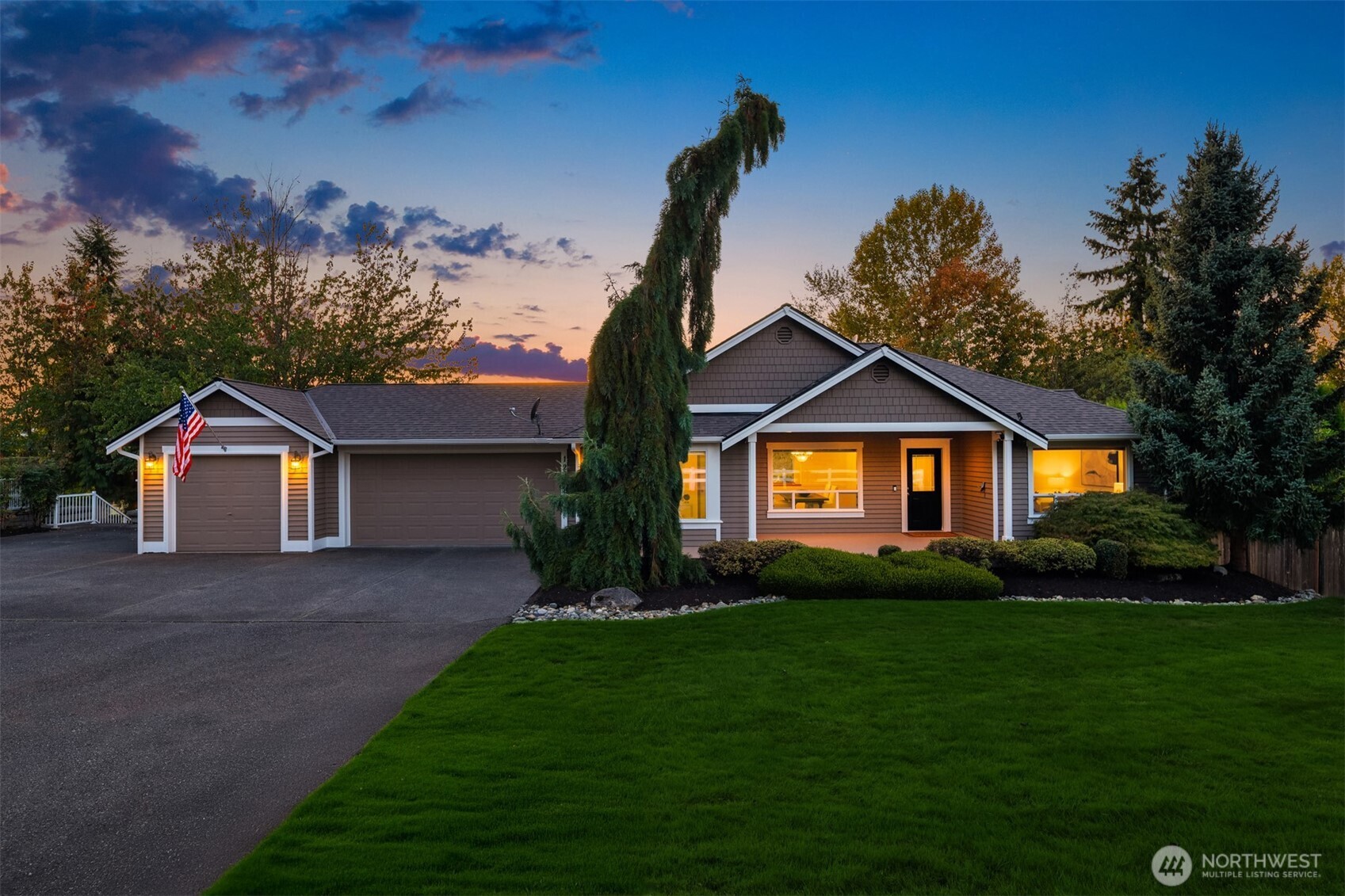 Single-story home at dusk with an attached two-car garage, warmly lit windows, and a broad driveway.