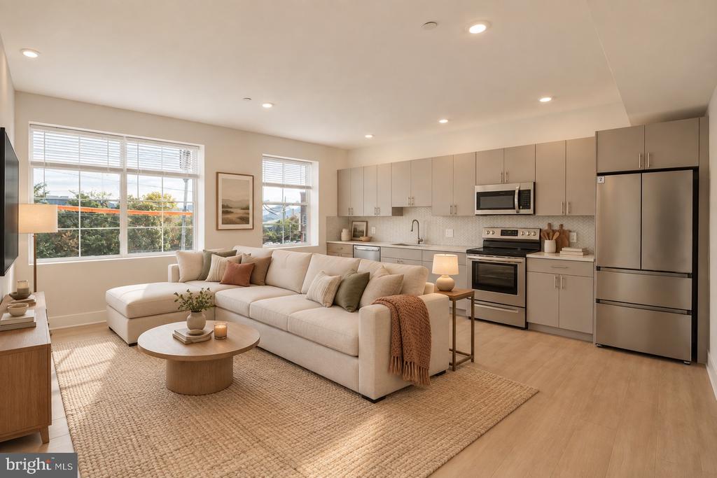 Open-plan living room and kitchen with a cream sectional, large windows, and stainless steel appliances.